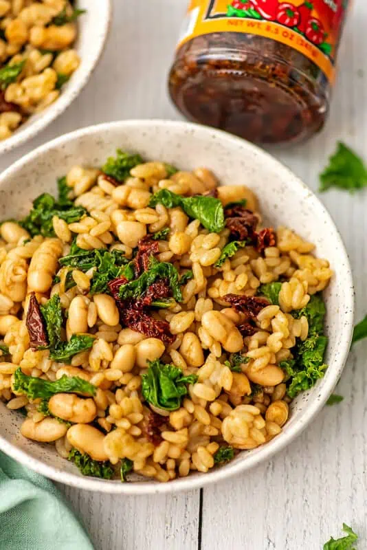 White bowl filled with sundried tomato orzo and kale.