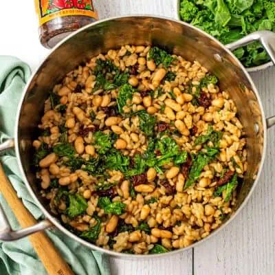 Tuscan orzo with kale and white beans in a stainless steel pot.