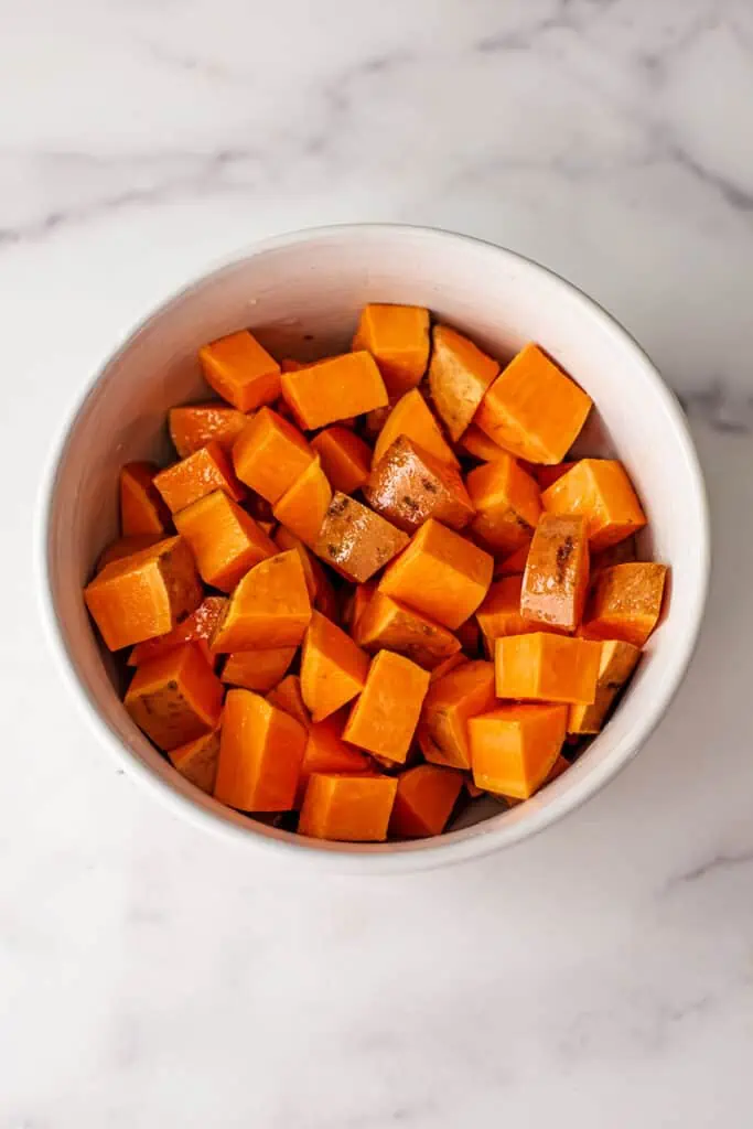Sweet potato cubes in white bowl with oil and salt on top.