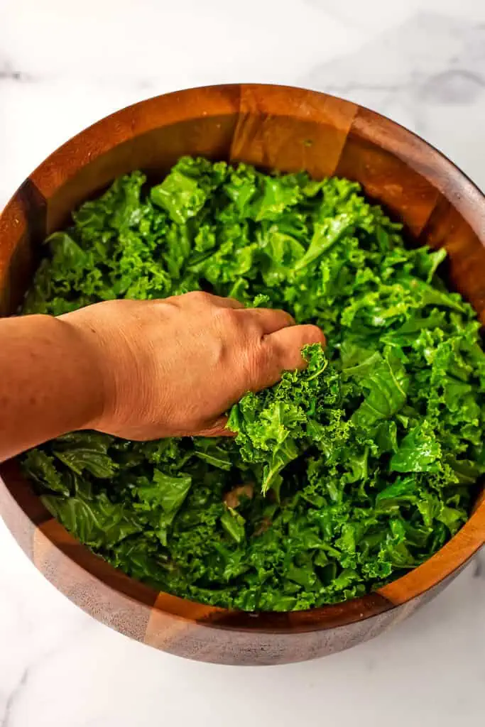 Hand massaging kale in wood salad bowl.