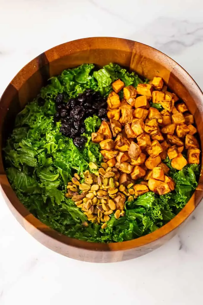 Kale, roasted sweet potatoes, cranberries and pistachios in wood salad bowl.
