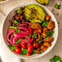Sweet potato black bean bowls filled with potatoes, beans, avocado, pickled onions and tomatoes.