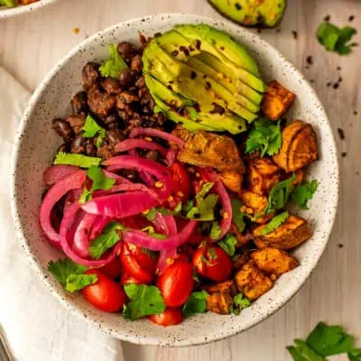 Sweet potato black bean bowls filled with potatoes, beans, avocado, pickled onions and tomatoes.