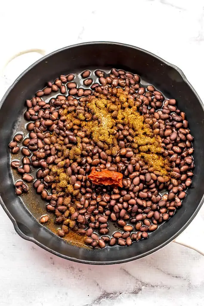 Tomato paste with spices over black beans in skillet.