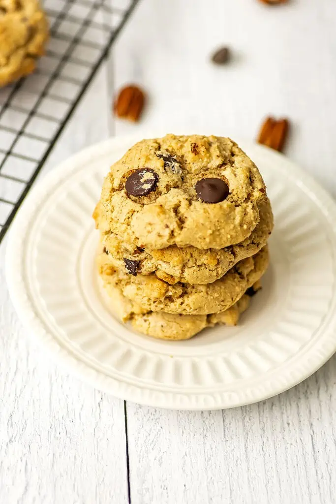 Four chocolate chip and pecan cookies stacked on a white plate.
