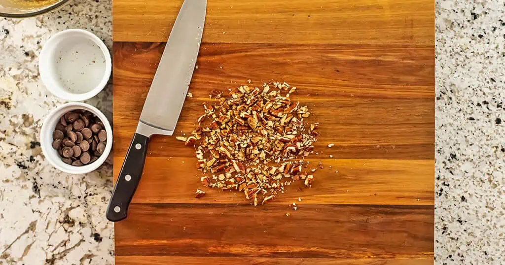 Chopped pecans on a cutting board with a knife on the side.