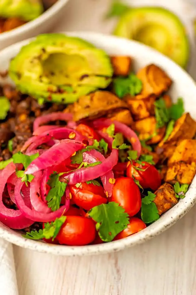 Sweet potato black bean bowls with sliced avocado, tomatoes and onions.