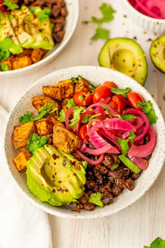 Sliced avocado over black beans and sweet potatoes in white bowl.