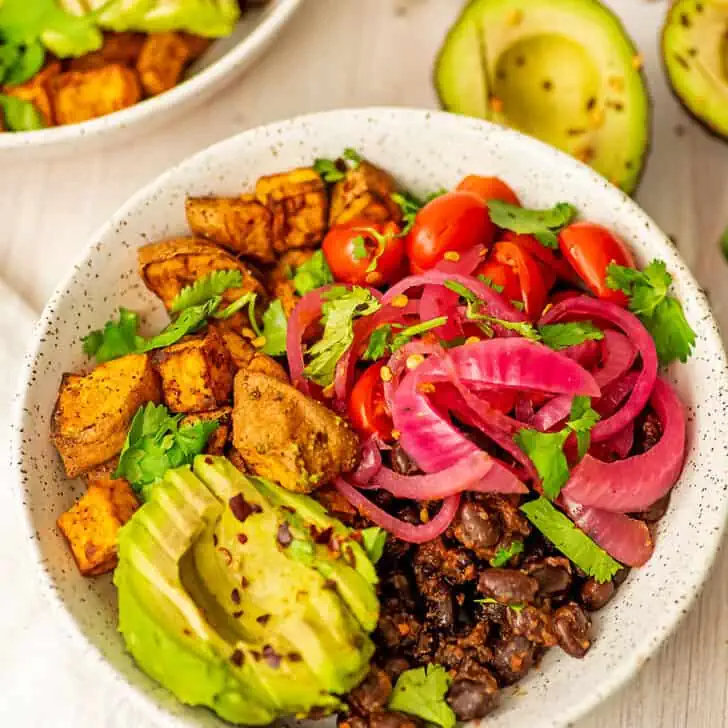 Sliced avocado over black beans and sweet potatoes in white bowl.