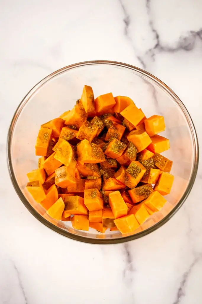 Sweet potato cubes in glass bowl with spices on top.
