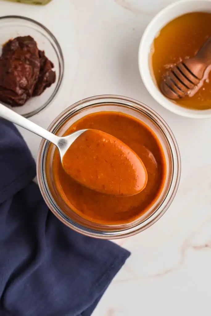 Spoonful of honey chipotle sauce over a jar of sauce, blue napkin on the side.