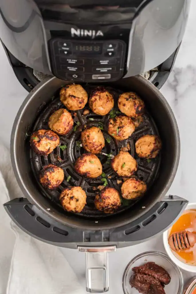 Chipotle turkey meatballs in air fryer basket, chipotle peppers and sauce on the side.