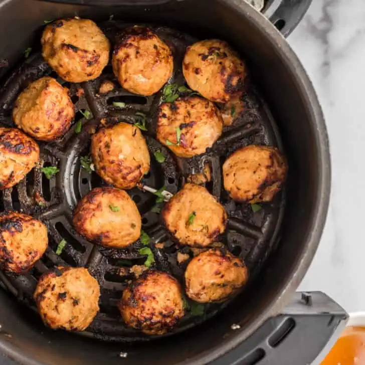 Air fryer basket filled with turkey meatballs, bowl of sauce on the side.