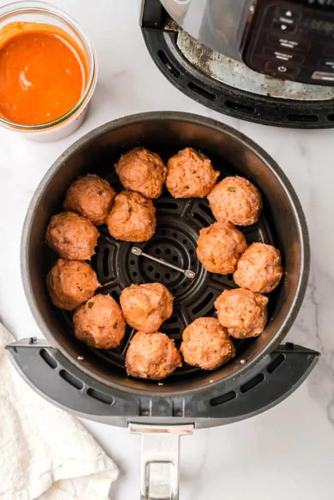 Ground turkey meatballs in air fryer basket before cooking.