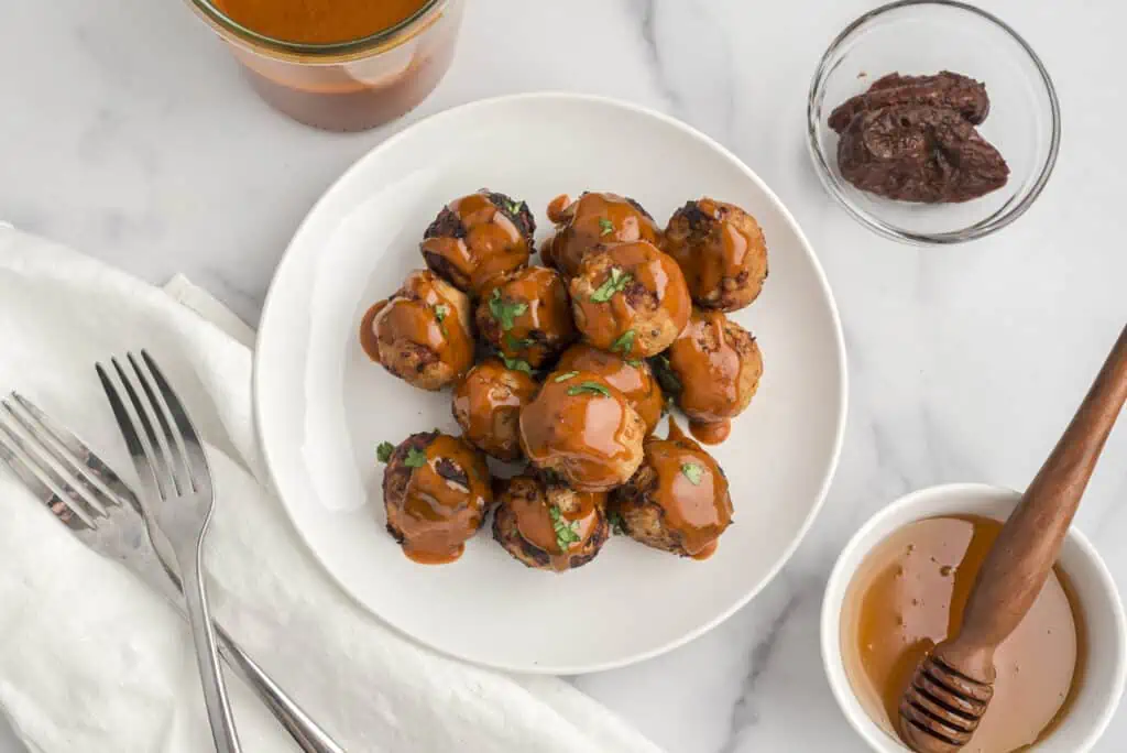 Air fryer ground turkey meatballs on a white plate with chipotle honey sauce on top.