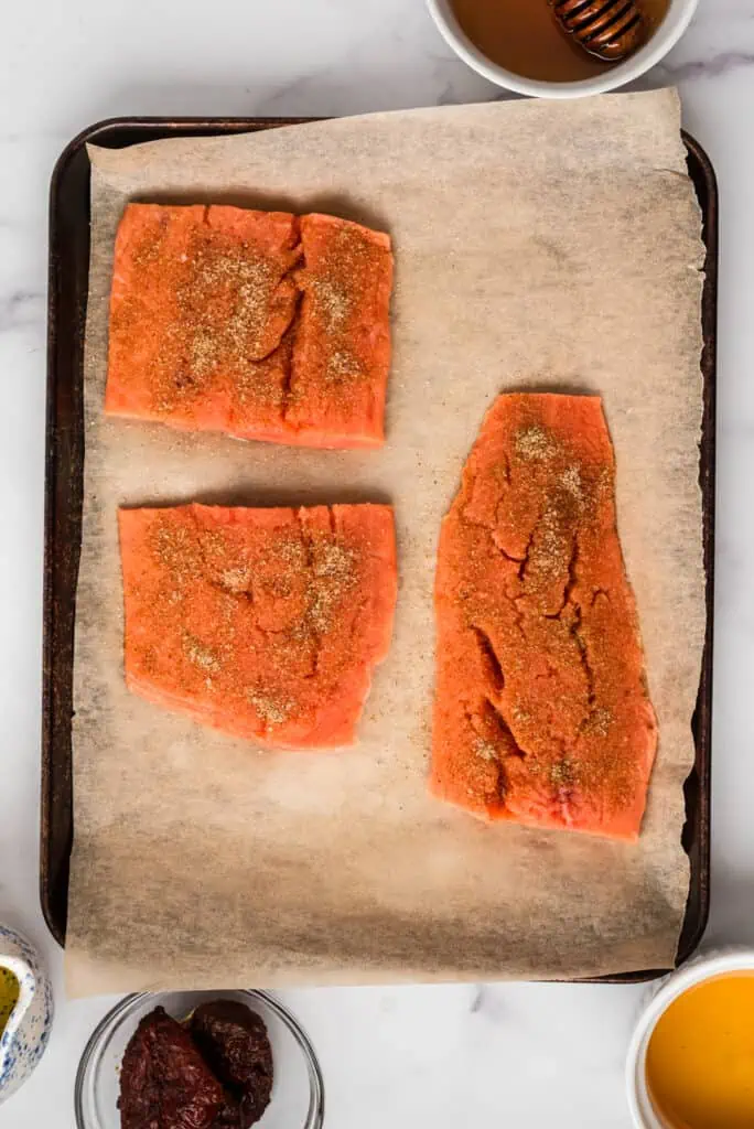 Raw salmon on sheet pan with salt, garlic powder and cumin on top.