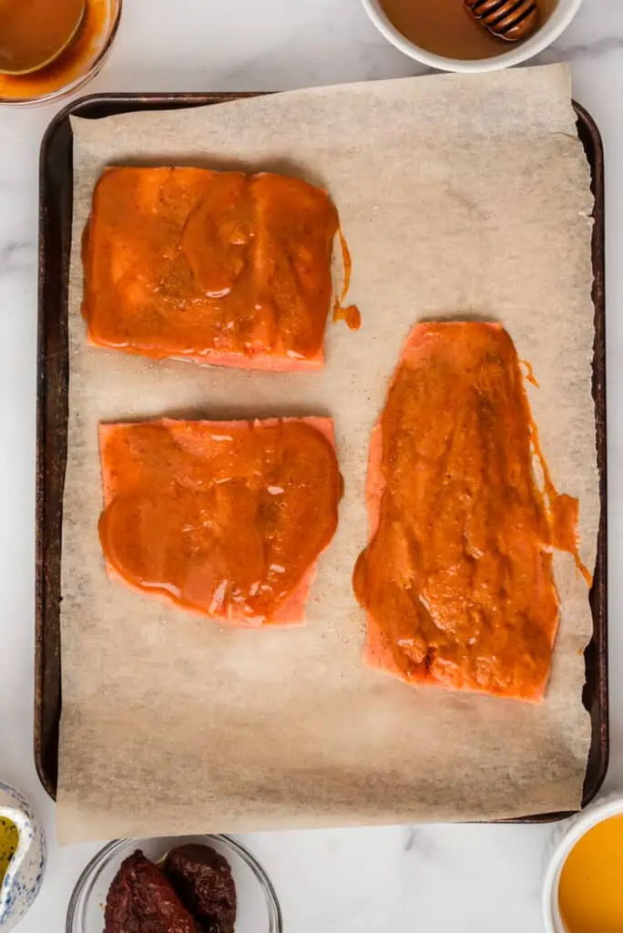 Raw salmon on sheet pan with honey chipotle sauce on top.
