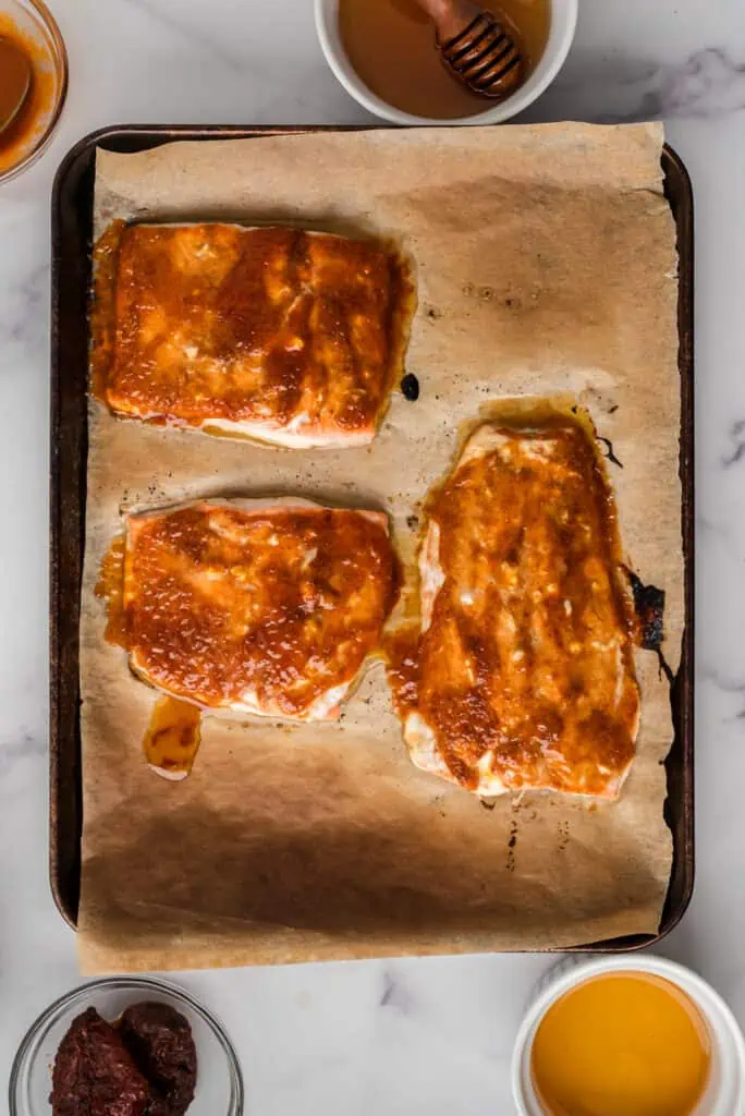 Salmon coated in honey chipotle sauce on parchment paper.