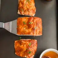 Honey chipotle salmon being lifted off baking sheet with spatula .