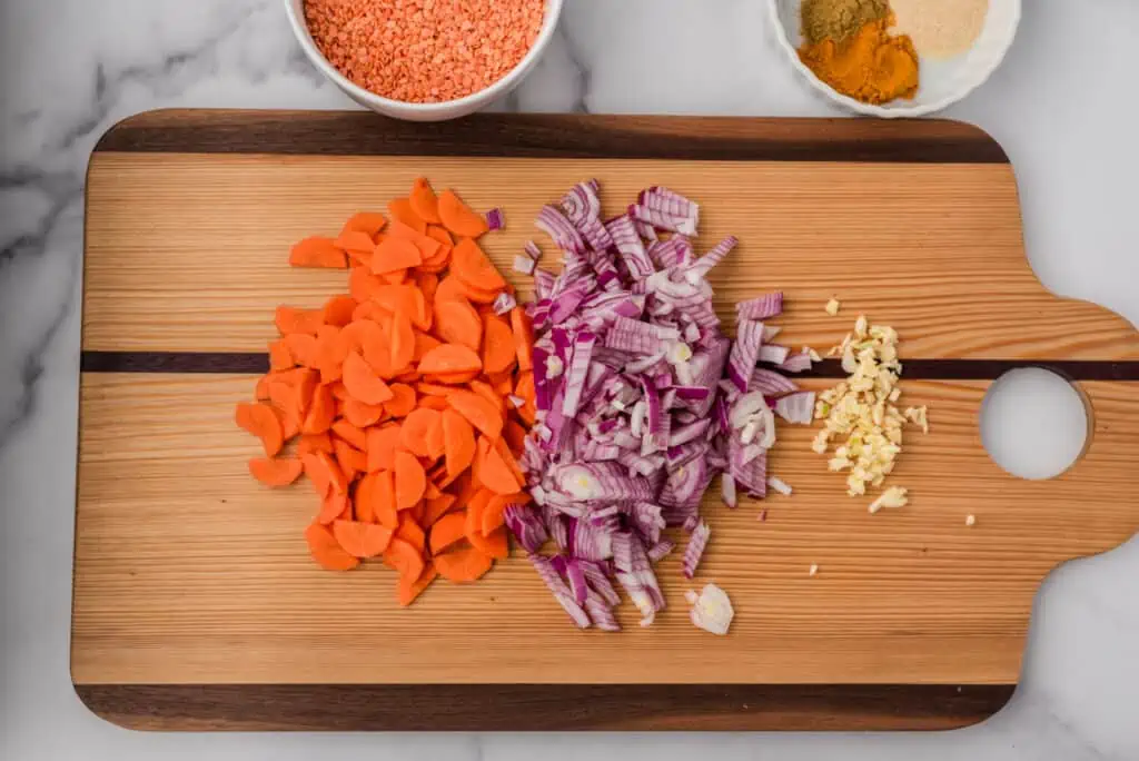 Sliced carrots, chopped red onion and garlic on a cutting board.