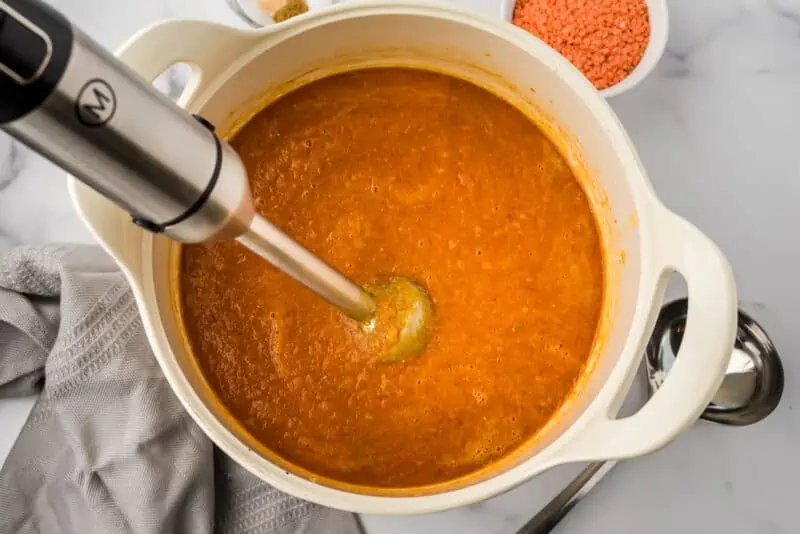 Pot of Moroccan lentil soup with immersion blender in the soup.