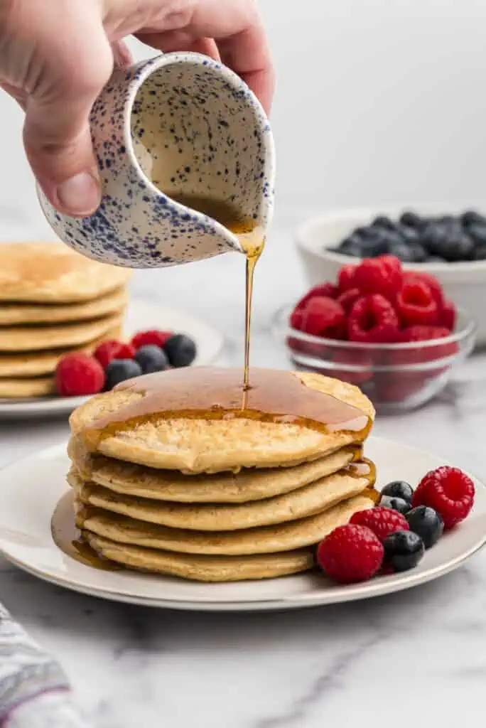 Maple syrup being poured on stack of oat flour pancakes.