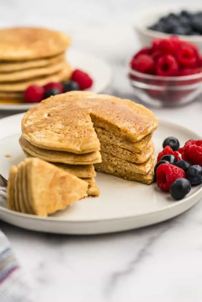 Oat flour pancakes stacked on white plate with a wedge cut out.