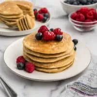 Oatmeal flour pancakes stacked on a white plate with fruit on top.