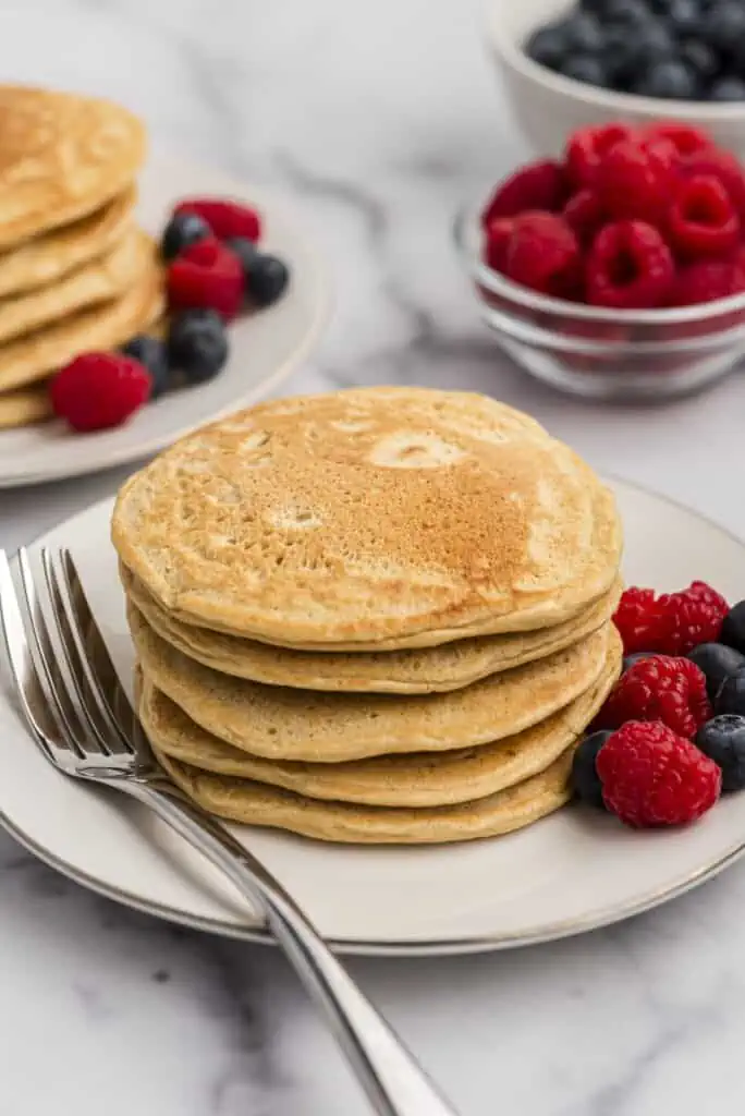 Stack of oat flour pancakes on a white plate, berries on the side.