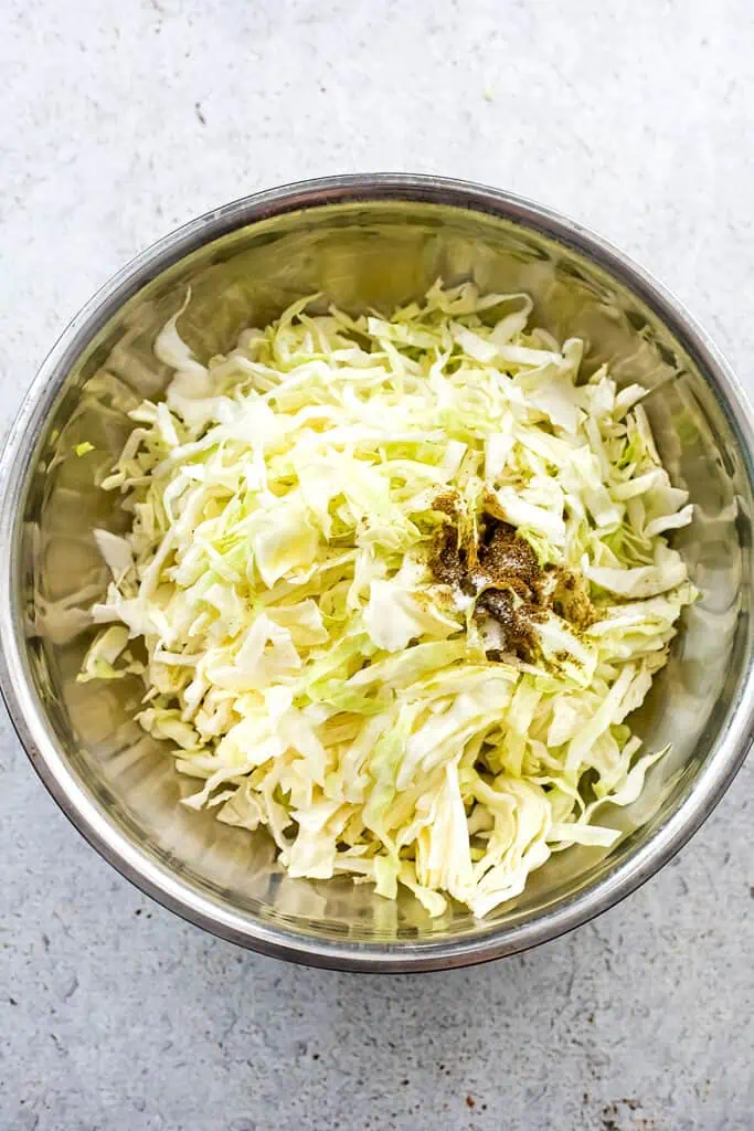 Stainless steel bowl with shredded cabbage and spices.