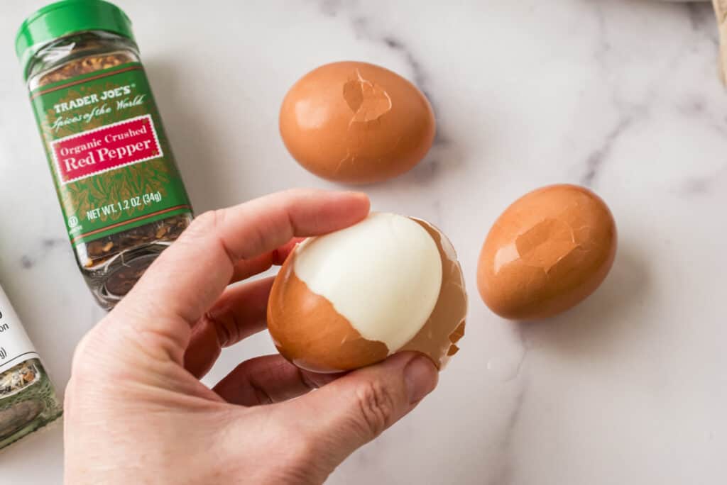 Hand holding hard boiled eggs with shell being removed.