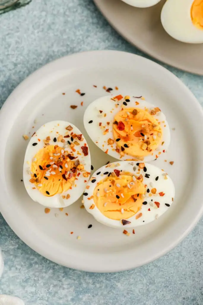 Three sliced hard boiled eggs on a white plate with everything seasoning on top.