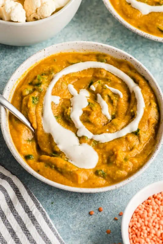 Bowl of cauliflower red lentil soup with a swirl of cashew cream in the bowl with spoon resting in the bowl.