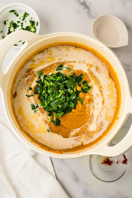 Dairy free milk and frozen spinach added to pot of creamy soup.