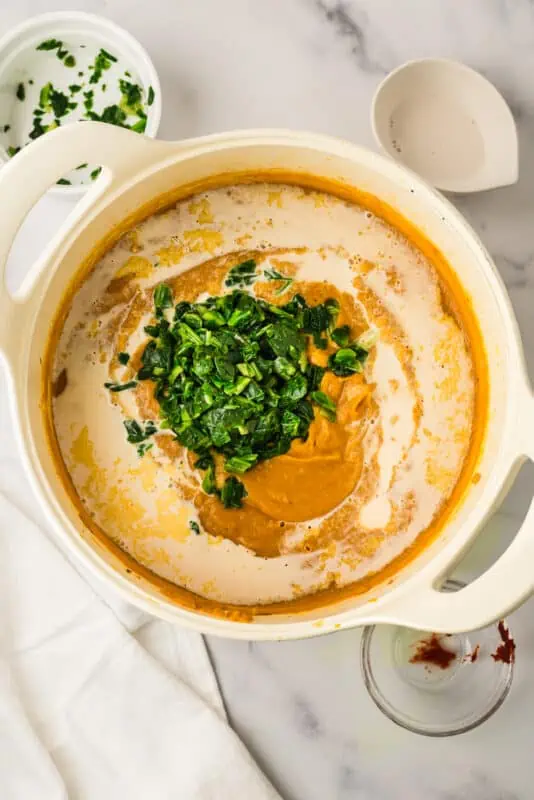 Dairy free milk and frozen spinach added to pot of creamy soup.