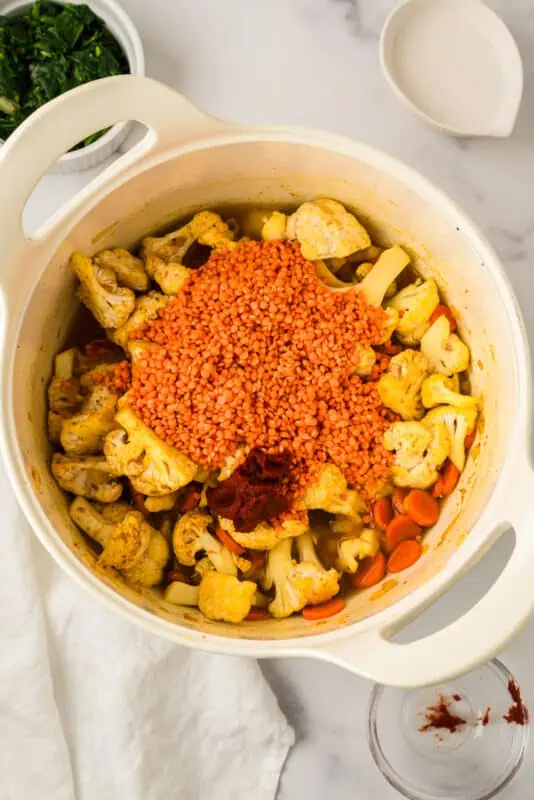 Red lentils, spiced cauliflower, broth and tomato paste in pot.