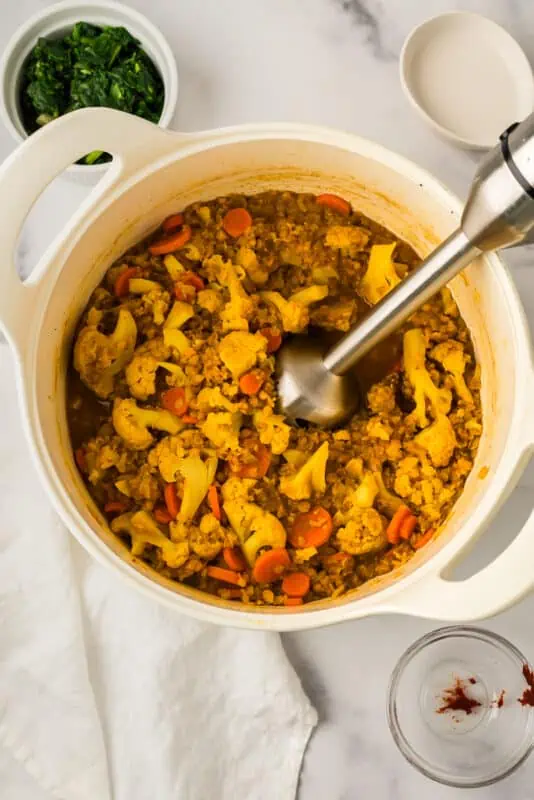 Immersion blender resting in pot with cooked cauliflower and lentils.