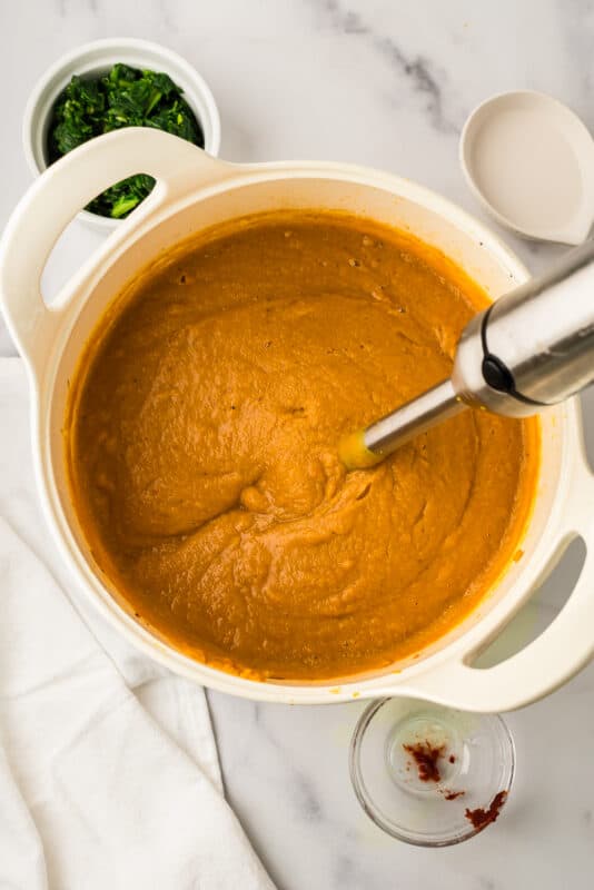 Creamy cauliflower red lentil soup with immersion blender resting in pot.