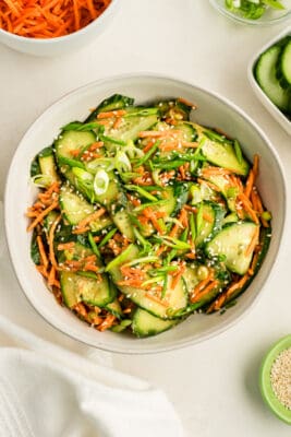 Sesame dressing over cucumber carrot salad in a white bowl.