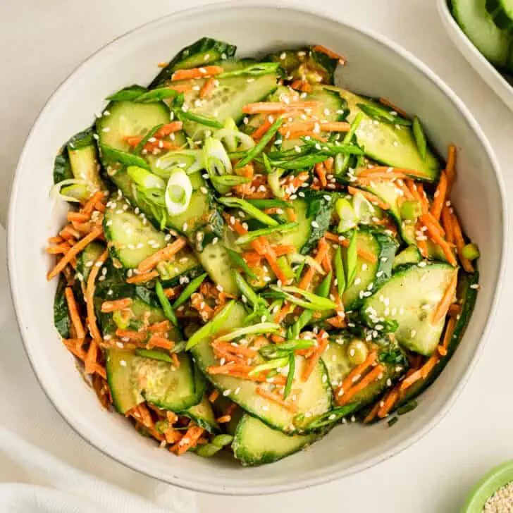Sesame dressing over cucumber carrot salad in a white bowl.