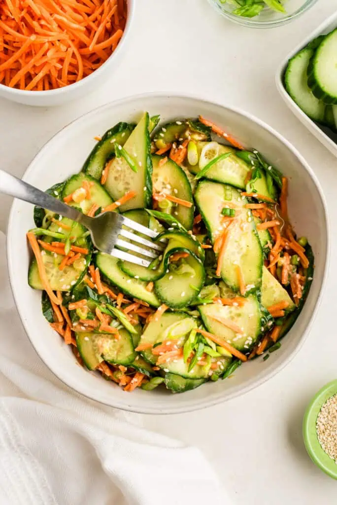 Fork resting in a bowl of Asian cucumber carrot salad.