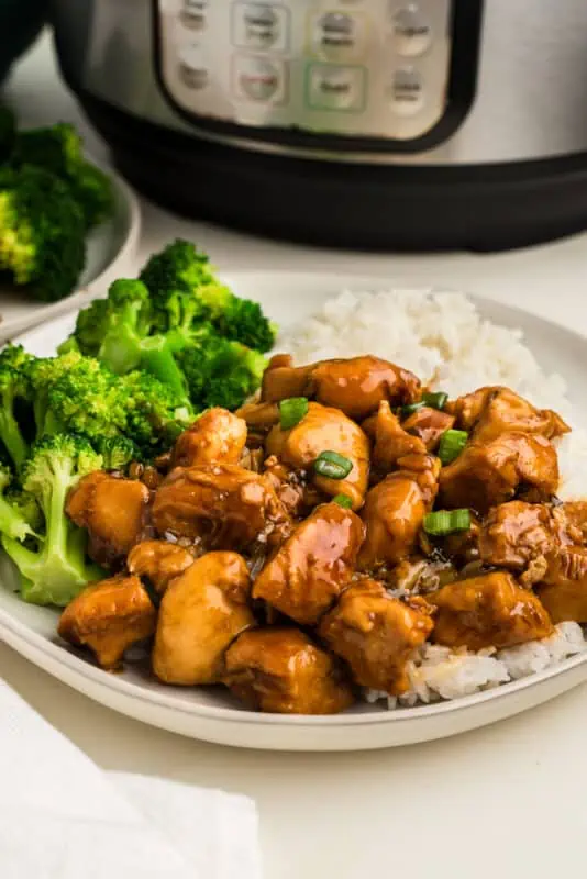 Healthy teriyaki chicken on plate with broccoli and rice, instant pot in background.