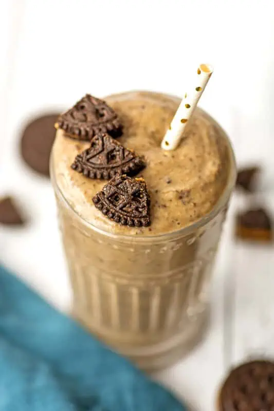 Oreo protein shake in a glass with pieces of cookie on top.