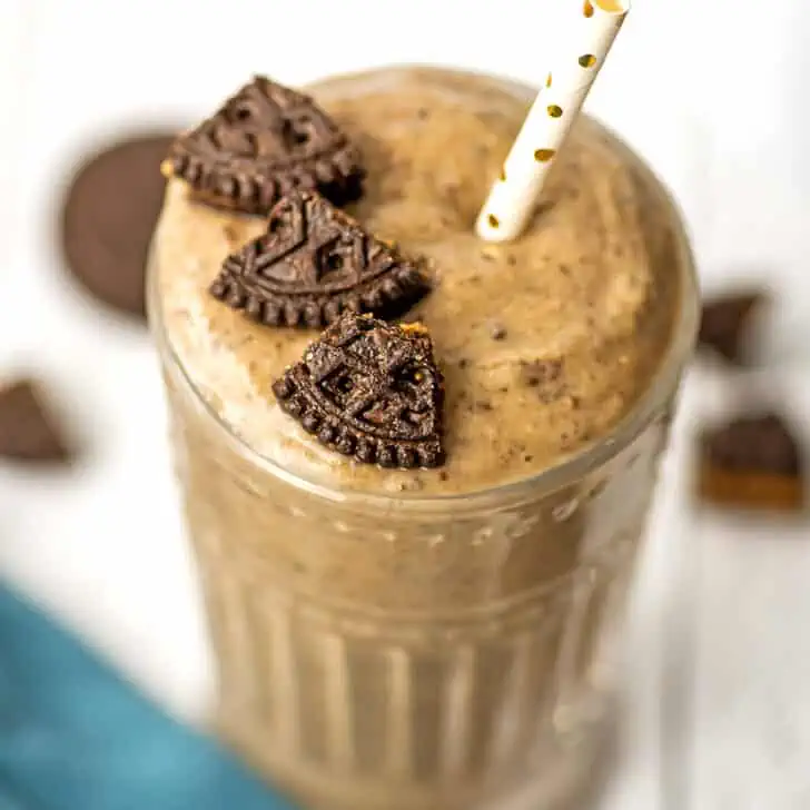 Oreo protein shake in a glass with pieces of cookie on top.