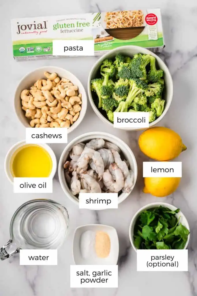 Ingredients to make broccoli and shrimp pasta in ramekins on marble countertop.