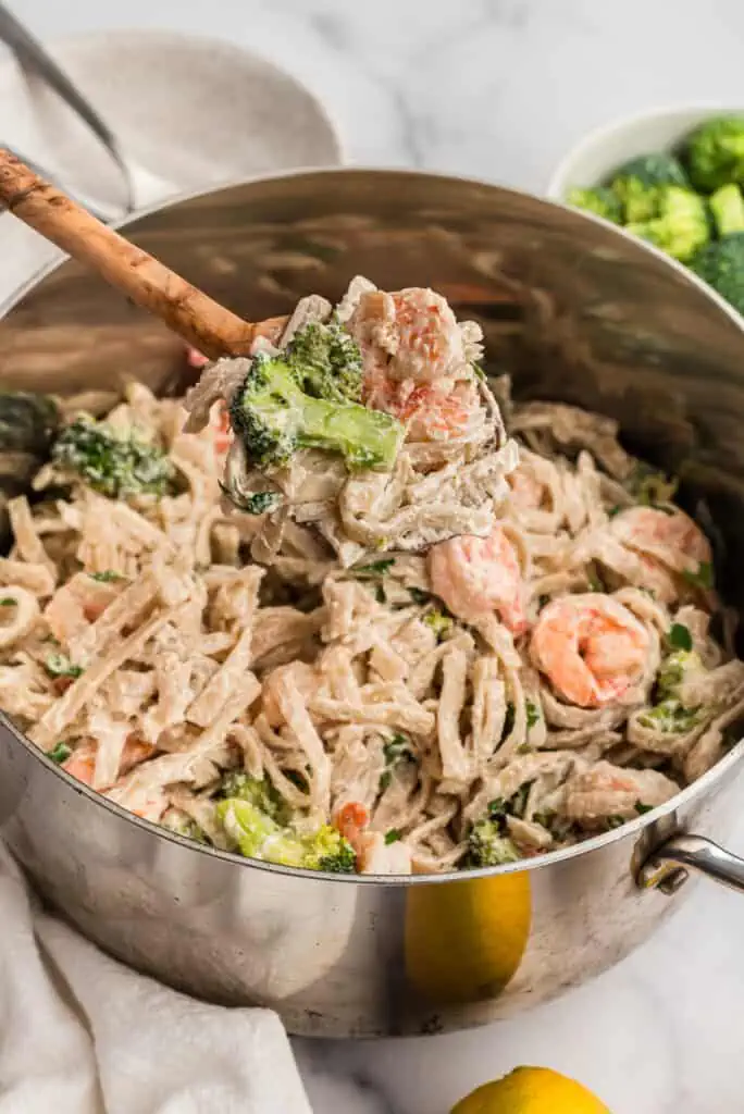 Broccoli shrimp pasta in a pot with a wood spoon scooping out the pasta.