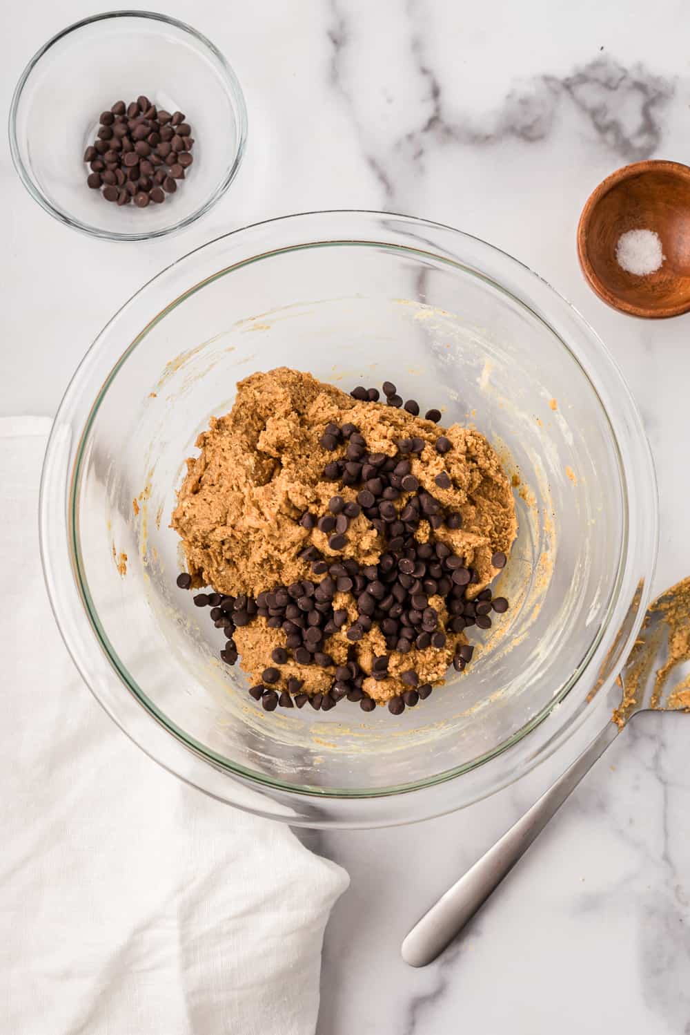 Chocolate chips added to almond butter protein mixture in glass bowl.