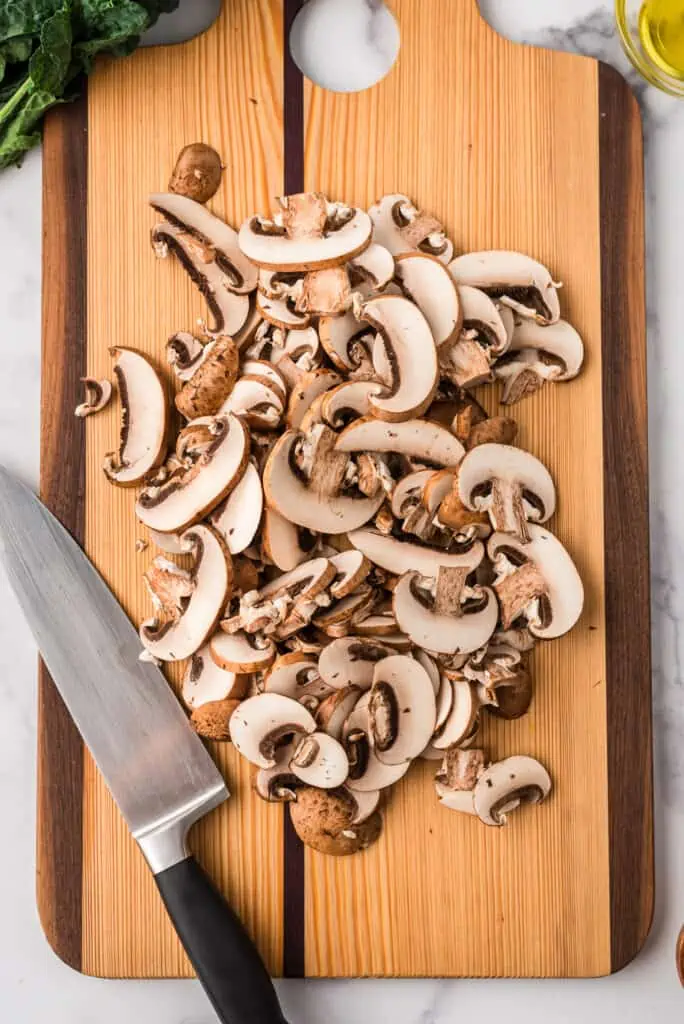 Sliced mushrooms on wood cutting board.