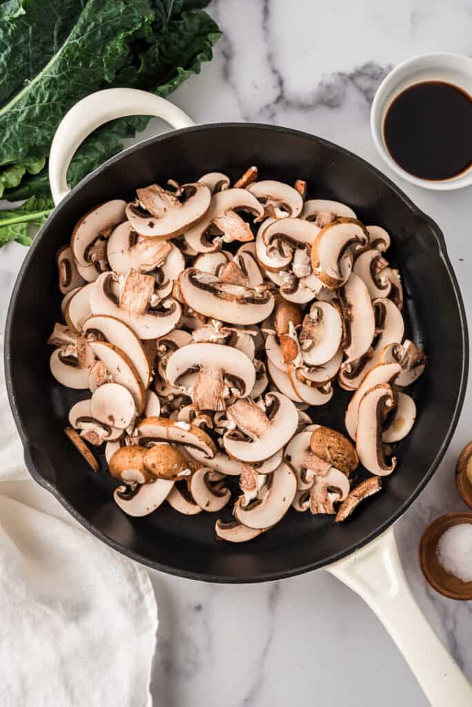 Sliced mushrooms in cast iron skillet before cooking.