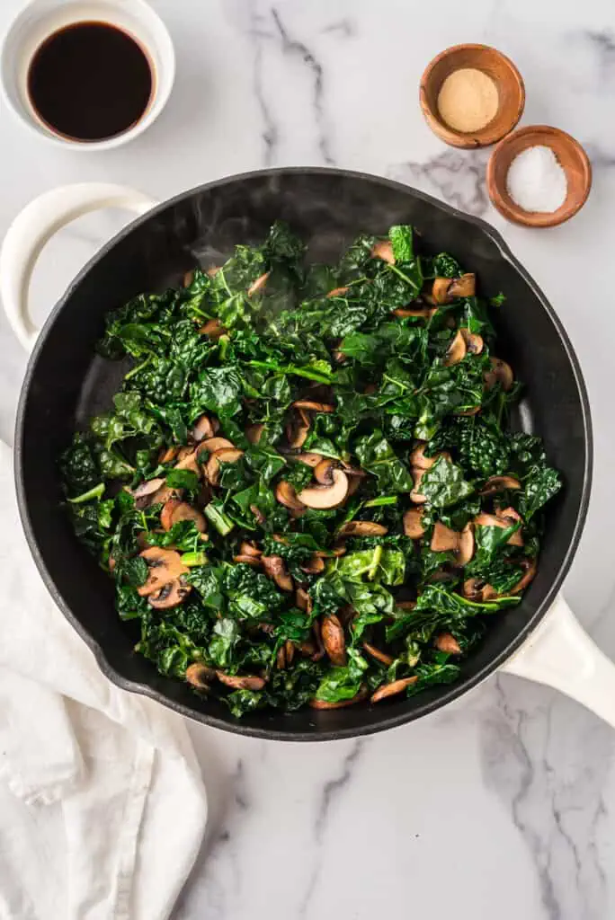 Saute pan filled with sauteed kale and mushrooms.